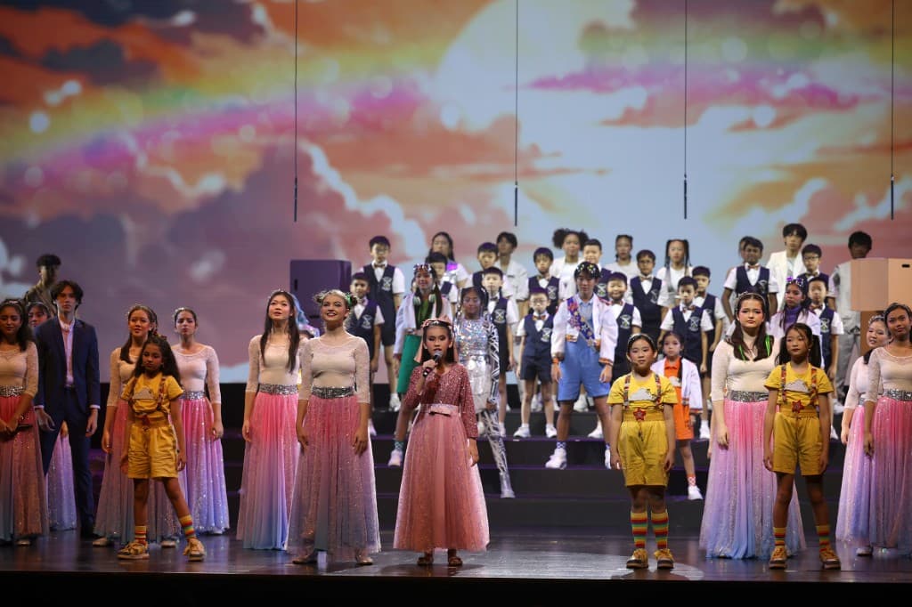 ChildAid ensemble of children on a wide stage against a colourful sunset rainbow backdrop