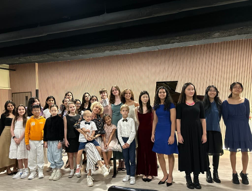 Large mixed-age cast posing on stage after a spring concert with grand piano behind