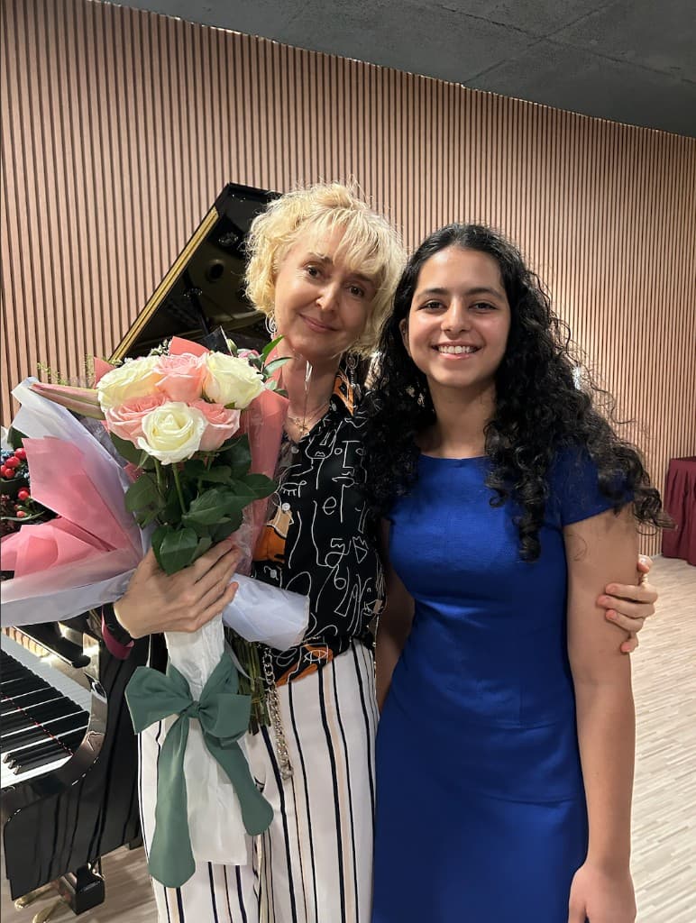 Tara in royal blue beside a mentor with roses, grand piano and wood-panel studio