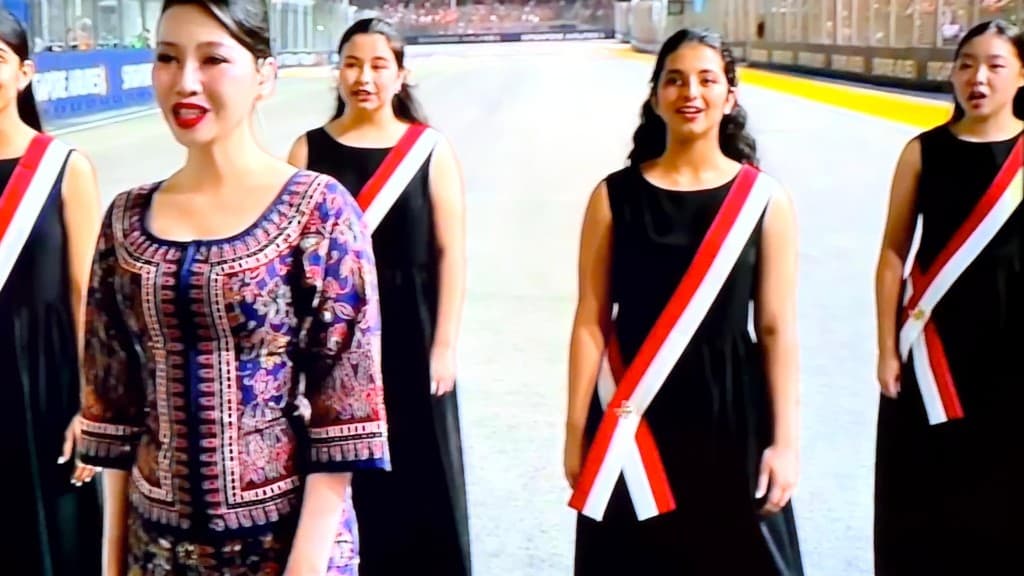 Singer in Singapore Airlines sarong kebaya with choir in sashes at F1 Singapore Airlines track signage