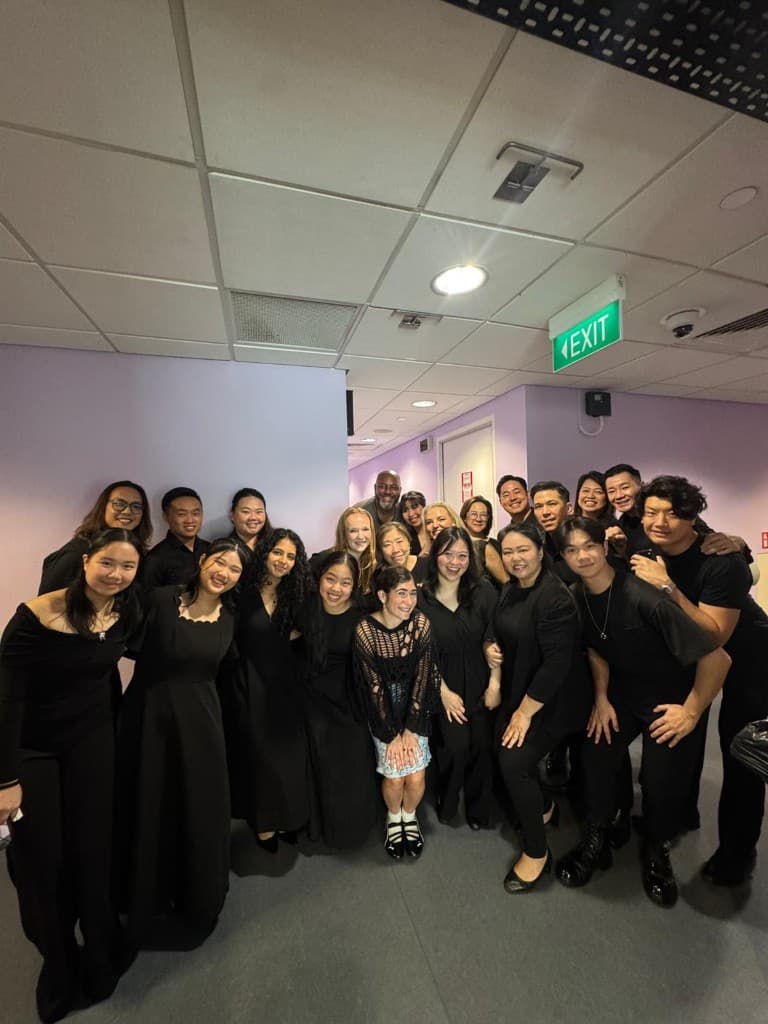 Ensemble singers in formal black posing together in a backstage corridor